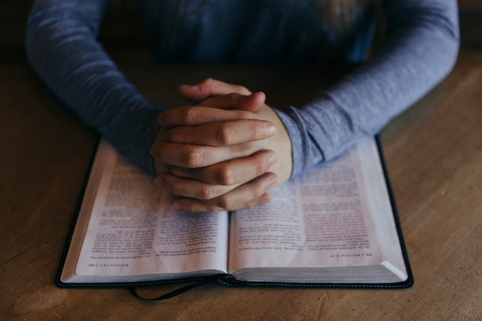 hands clasped on an open Bible